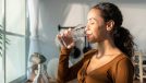 woman drinking water in bright kitchen, concept of how much water to drink for weight loss